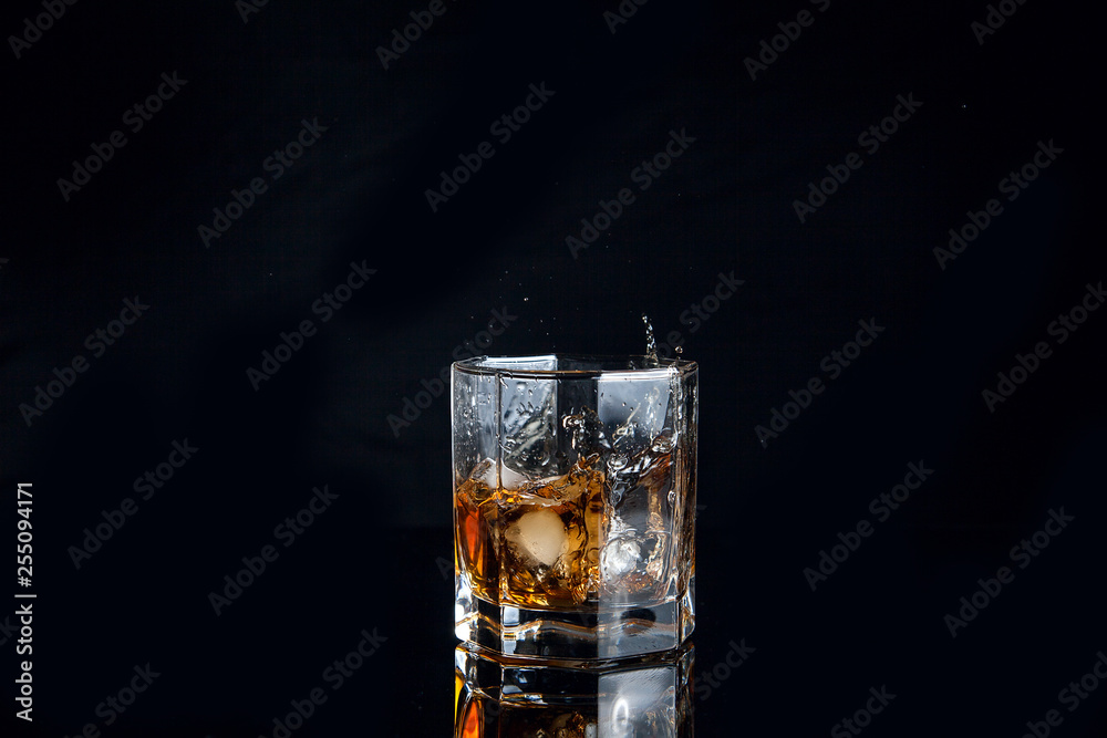 Whiskey splash from the fallen ice cube into glass with beverage isolated on black background.. Whiskey splash from the fallen ice cube into glass with beverage isolated on black background..