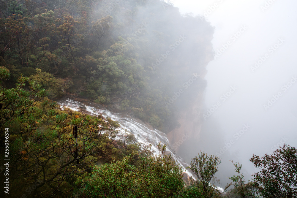 Waterfall flows off the cliff into the foggy abyss