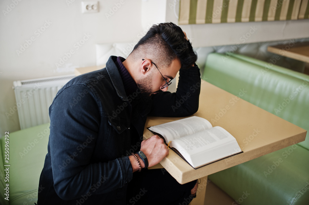 Arab man wear on black jeans jacket and eyeglasses sitting in cafe, read book. Stylish and fashionable arabian model guy. Arab man wear on black jeans jacket and eyeglasses sitting in cafe, read book. Stylish and fashionable arabian model guy.