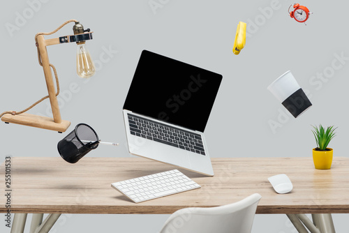 laptop with blank screen and stationery levitating in air at workplace isolated on grey