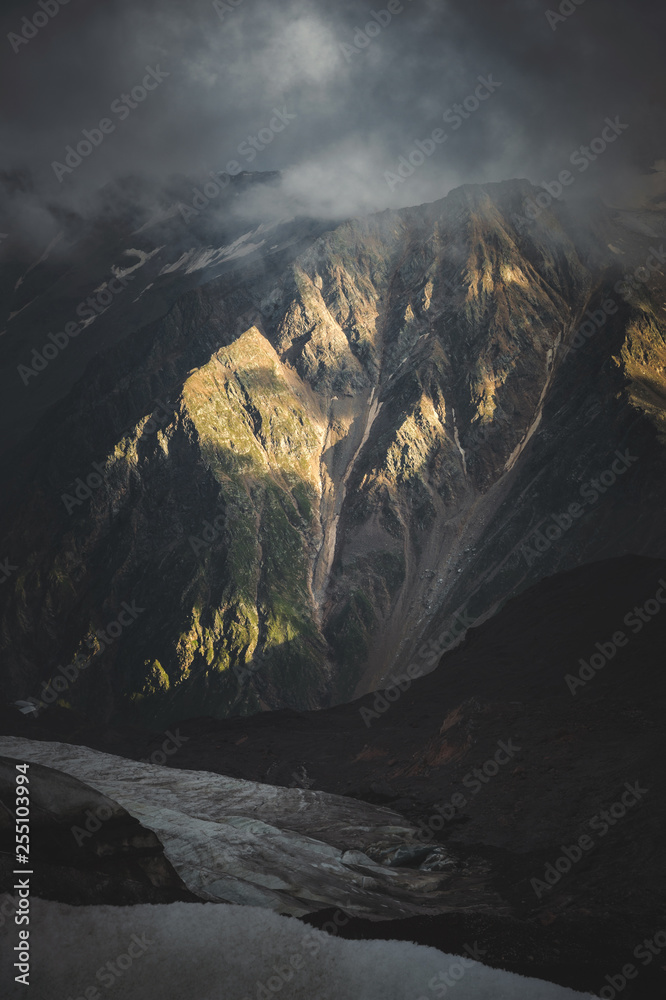 Low evening sunlight at sunset illuminates the sharp rocky ridges of the high stone walls of the Caucasus Mountains in the North Caucasus