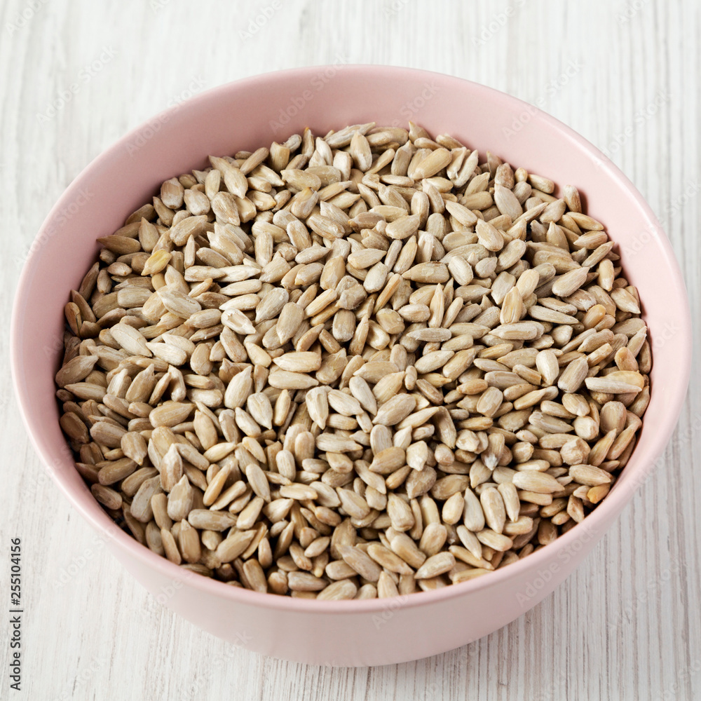 Dry hulled sunflower seeds in a pink bowl over white wooden background, low angle view. Closeup.