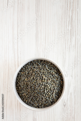 Top view, organic green french lentils in gray bowl over white wooden surface, top view. Flat lay, overhead, from above. Copy space.