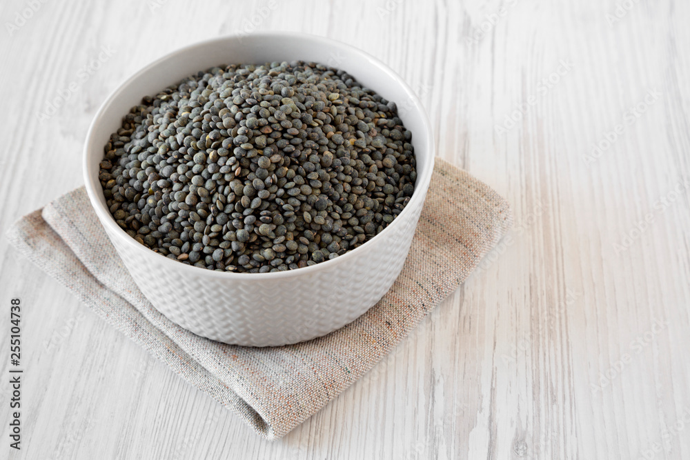 Dry green french lentils in gray bowl over white wooden background, low angle view. Close-up. Dry green french lentils in gray bowl over white wooden background, low angle view. Close-up.