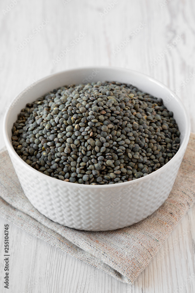 Green french lentils in gray bowl over white wooden background, low angle view. Close-up. Green french lentils in gray bowl over white wooden background, low angle view. Close-up.
