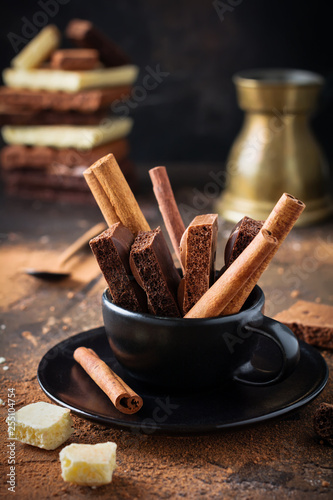 Slice of bitter, milky, porous, airy chocolate and cinnamon in black ceramic cup over dark old background. Selective focus.