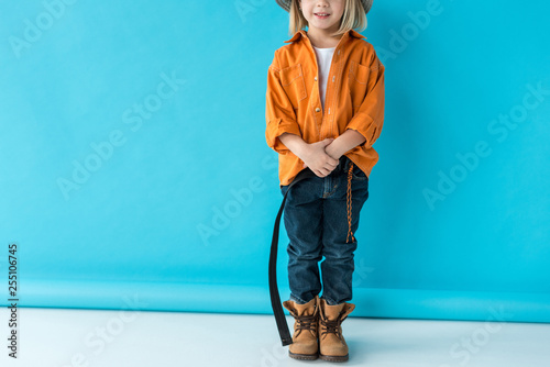cropped view of kid in jeans and orange shirt on blue background