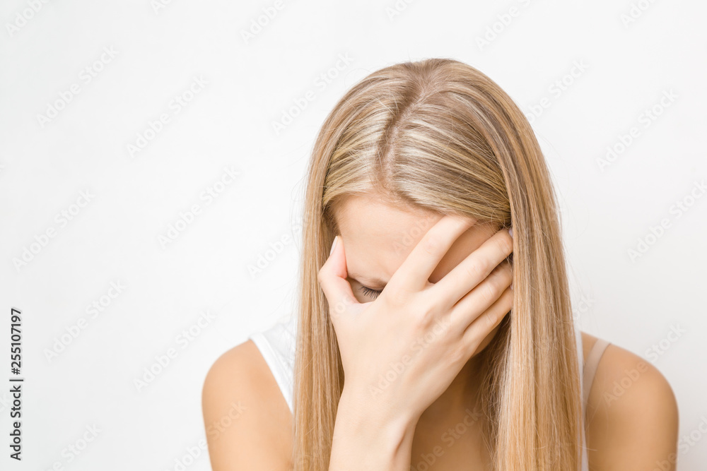 Young, adult blonde lady covering her face with hand and trying to calm down. Nervous woman touching head. Memory disorder. Women's issues. Face close up on gray background. Young, adult blonde lady covering her face with hand and trying to calm down. Nervous woman touching head. Memory disorder. Women's issues. Face close up on gray background.