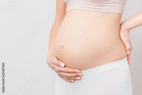 Wallpaper Mural Young woman hand touching naked big belly isolated on gray background. Emotional loving pregnancy time - 20 weeks. Baby expectation. Love, happiness and safety concept. Closeup. Front side view.  Torontodigital.ca