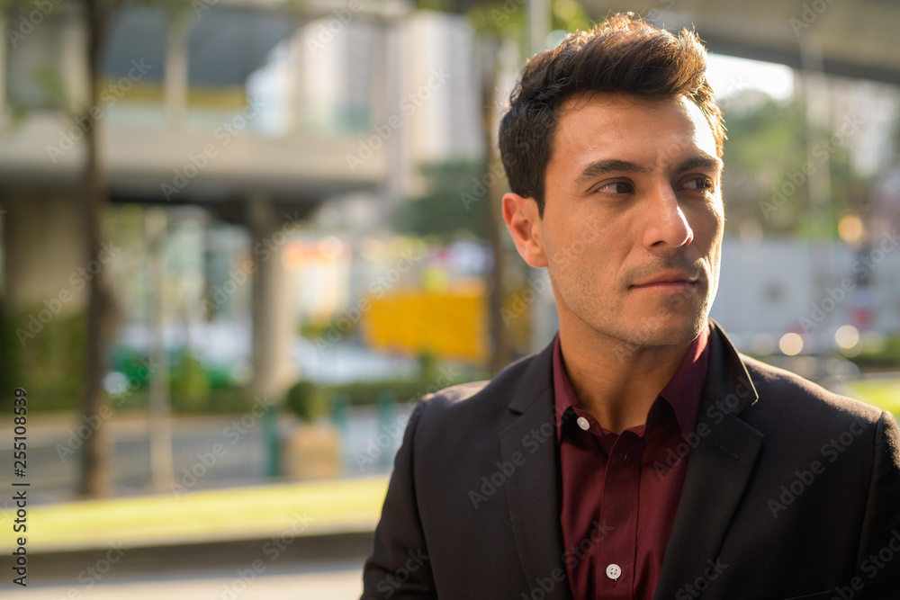 Face of young handsome Hispanic businessman thinking outdoors