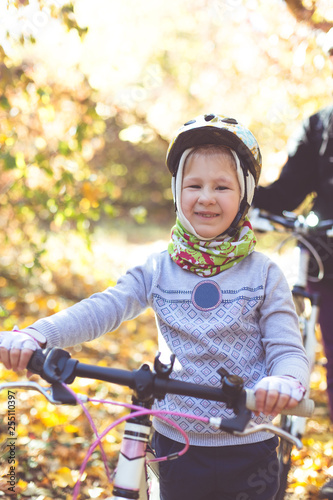 Little girl in the helmet with the bicycle in the autumn forest