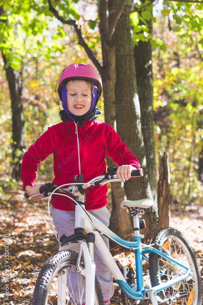 Naklejka premium Cute little girl with a bicycle in the autumn forest