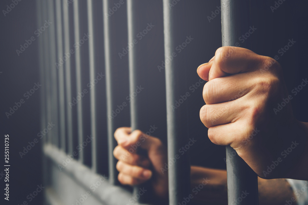 Man in prison hands of behind hold Steel cage jail bars. offender