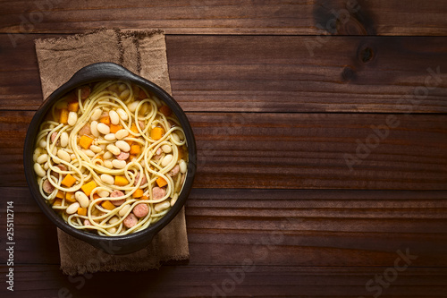 Chilean traditional Porotos con Riendas (beans with reins) dish of cooked dried beans with pumpkin, onion, spaghetti and sausage, photographed overhead on dark wood with natural light photo