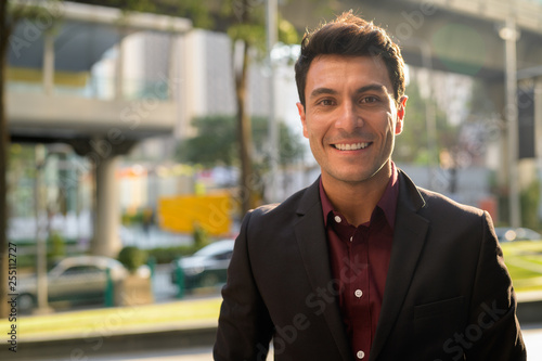 Face of happy young handsome Hispanic businessman smiling in the city photo