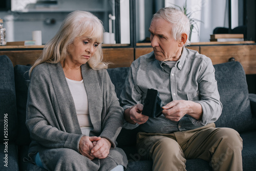 sad senior couple sitting on couch and holding wallets at home