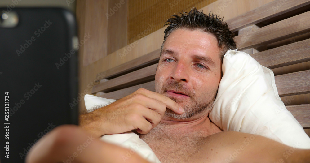 lifestyle portrait of young attractive and happy man lying on bed at home bedroom using mobile phone enjoying internet social media app or online gambling and dating lifestyle portrait of young attractive and happy man lying on bed at home bedroom using mobile phone enjoying internet social media app or online gambling and dating