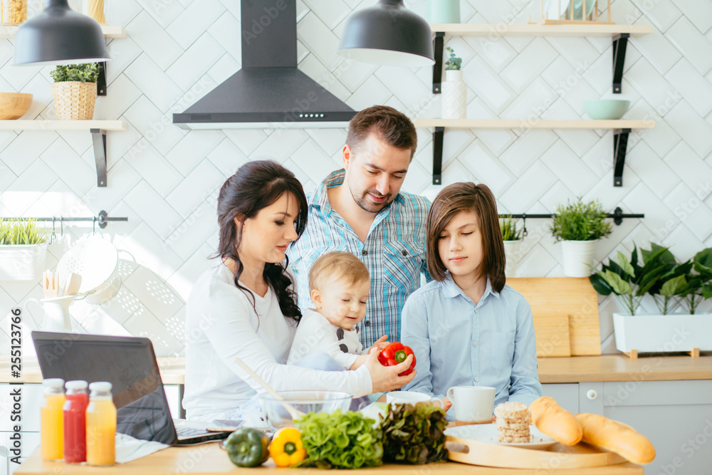 Young mother, father and two children cooking in a kitchen. Parents and kids cook dinner. Family with baby and school age kid eat at home. Child preparing and eating vegetable lunch.