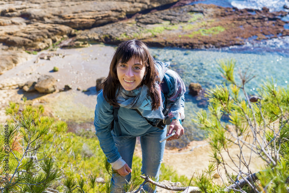 Above view of a young woman wearing casual clothes standing on the beach while looking to camera in a bright day