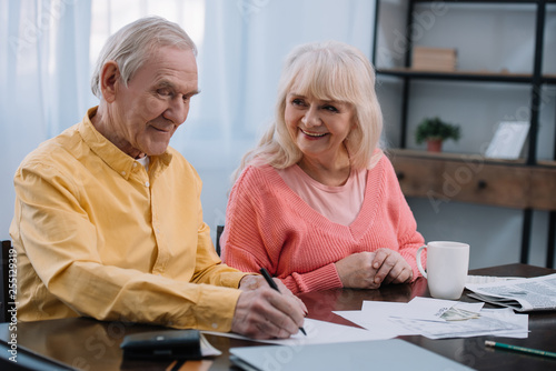 happy senior couple sitting at table and filling documents at home