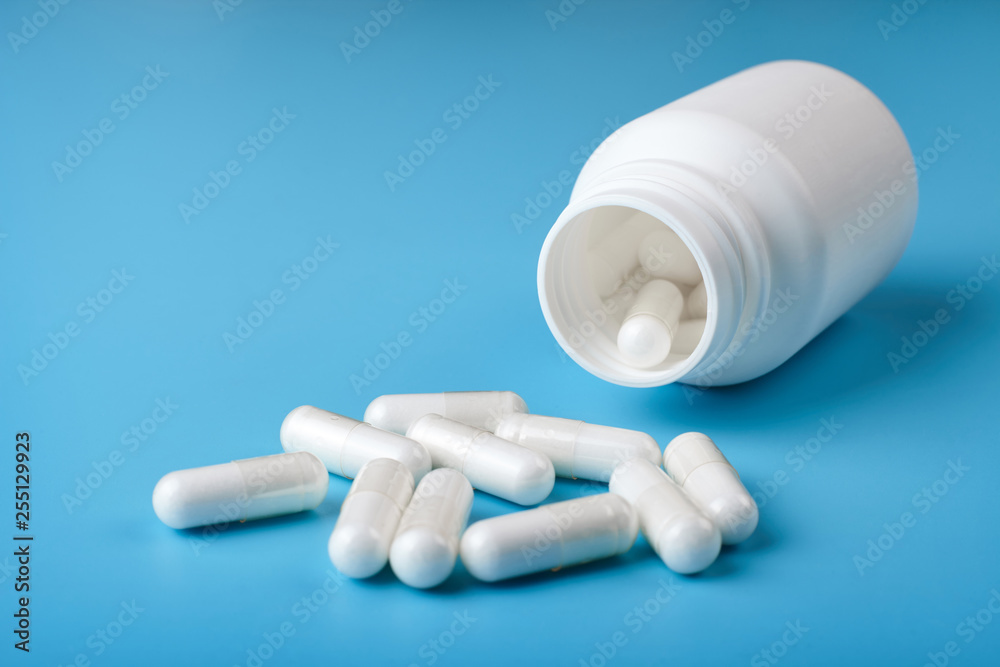 White pills and white bottle on blue background. White pills and white bottle on blue background.