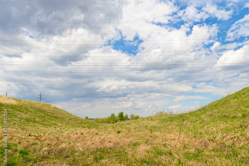 Spring landscape with a ravine and wires of power lines against the sky with clouds