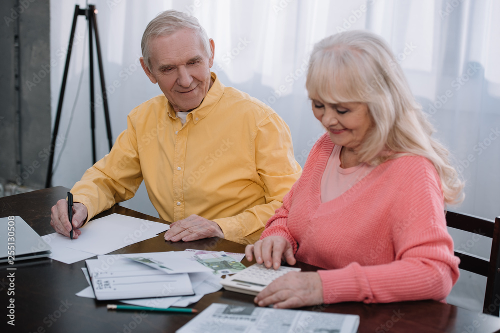 senior coupe sitting at table with calculator and counting money senior coupe sitting at table with calculator and counting money