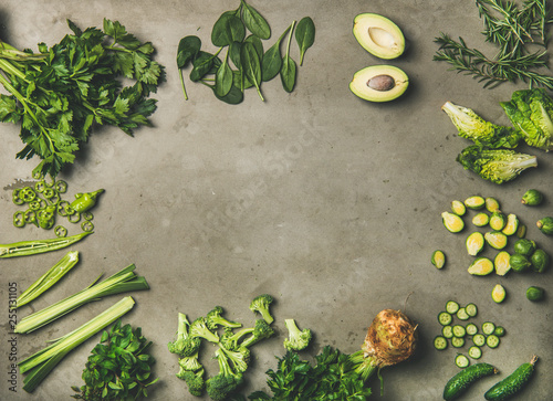 Healthy vegan ingredients layout. Flat-lay of whole and cut green vegetables and herbs over concrete background, top view, copy space. Vegetarian, clean eating concept