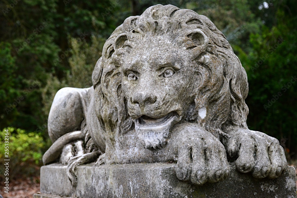 Lying stone lion statue, staring forward, placed on stone pedestal as guardian in botanical garden Lying stone lion statue, staring forward, placed on stone pedestal as guardian in botanical garden