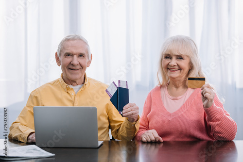 senior couple with air tickets, passports and credit card siiting at table with laptop and looking at camera © LIGHTFIELD STUDIOS