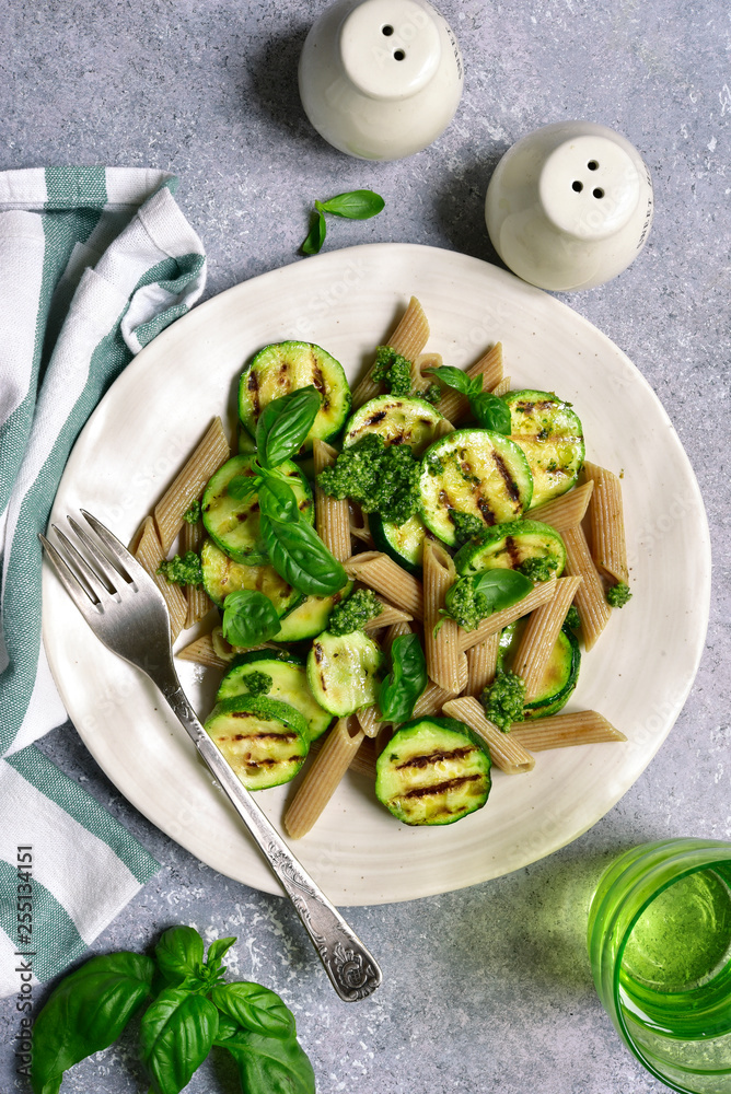 Whole grain spring penne pasta with grilled zucchini and basil pesto.Top view with copy space. Whole grain spring penne pasta with grilled zucchini and basil pesto.Top view with copy space.