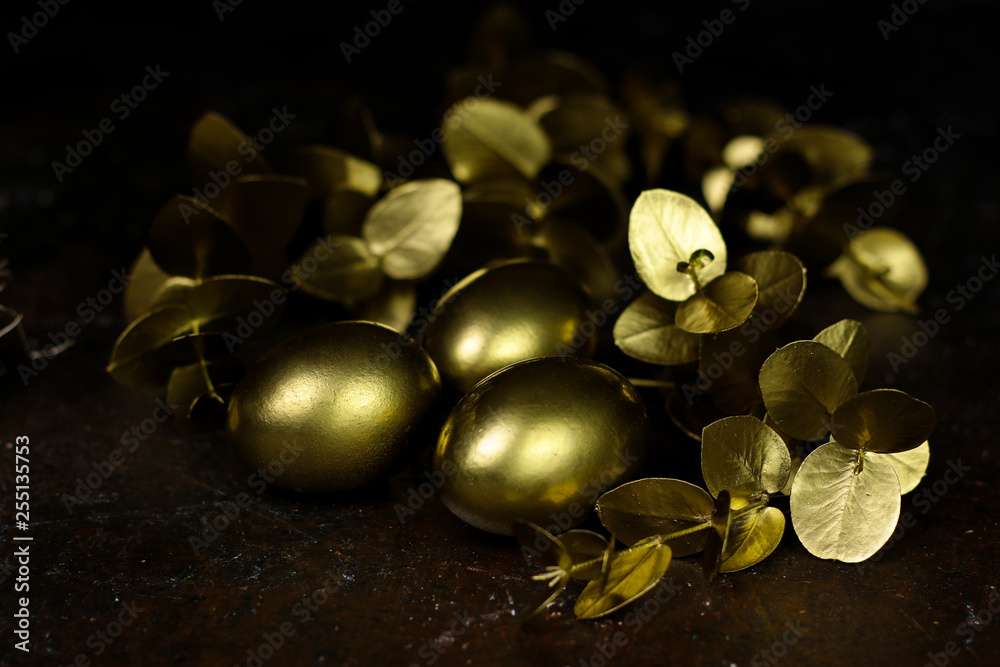 Golden eggs and golden decorative leafs.  Golden eggs on dark vintage wooden background.