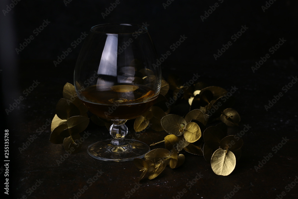 Glass with alcohol and golden floral design elements. Cognac Decanter on dark background. Carafe of brandy. Luxury concept.