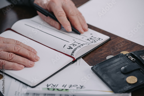 cropped view of senior woman holding pen near notebook with roth ira and traditional ira words