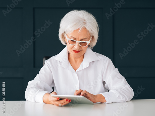 Smart senior woman portrait. Business intelligence. Elderly lady at workplace using wireless tablet access to data. photo