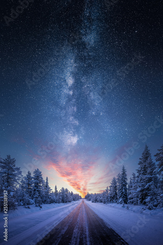 Fototapete Road leading towards colorful sunrise between snow covered trees with epic milky