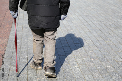 Man with walking cane on the street, rear view. Concept of limping or blind person, disability, old age, diseases of the spine