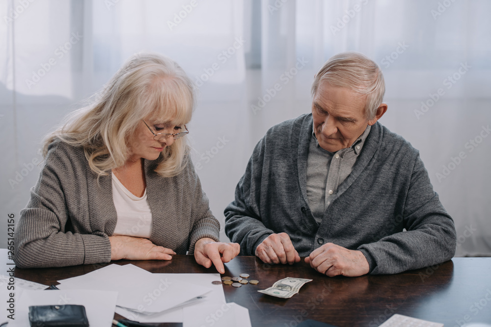 senior couple sitting at table with paperwork while counting money at home senior couple sitting at table with paperwork while counting money at home
