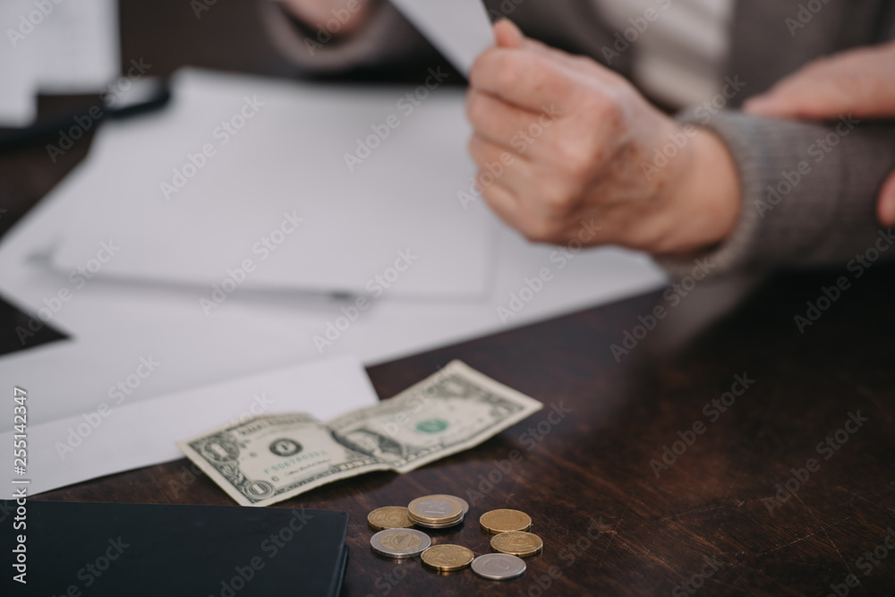 cropped view of senior woman sitting at table with paperwork, coins and banknote cropped view of senior woman sitting at table with paperwork, coins and banknote