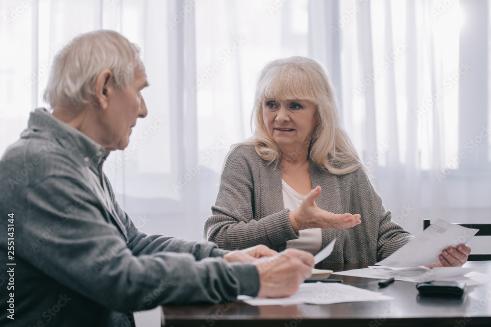 senior couple in casual clothes sitting at table and holding bills senior couple in casual clothes sitting at table and holding bills