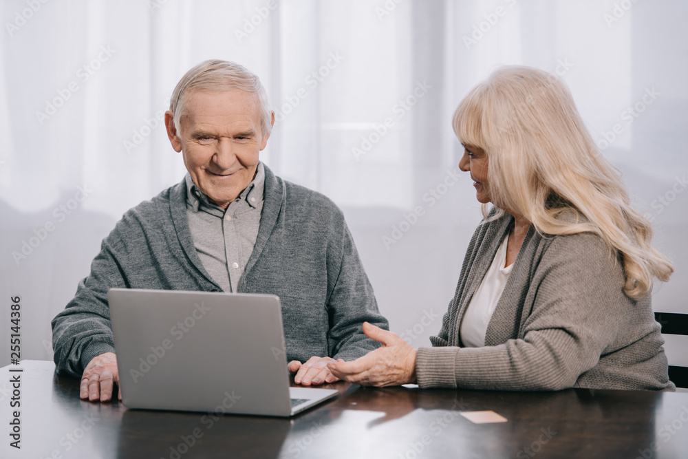 senior couple sitting at table and using laptop at home senior couple sitting at table and using laptop at home