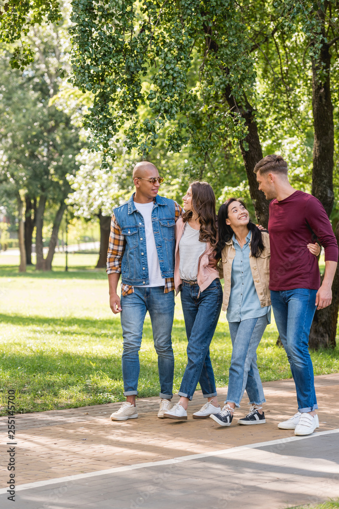 happy multiethnic friends hugging while walking together in park happy multiethnic friends hugging while walking together in park