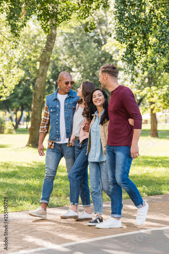smiling multiethnic friends hugging while walking together in park