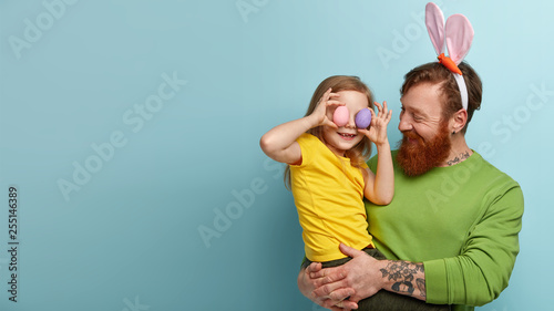 Look forward to celebrating Easter. Lovely family of daughter and father have eggs hunt, glad spring is coming. Satisfied red haired man carries little child who covers ears with colored eggs