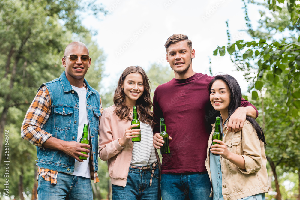 cheerful multicultural group of friends holding bottles with beer and looking at camera