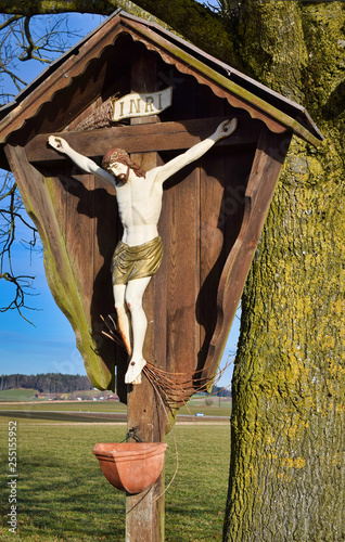 Feldkreuz in Oberbayern, vor Baum und Sitzbank, mit Weihwasserbehälter, im späten Winter photo