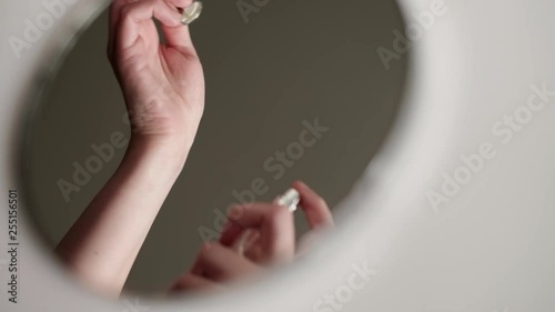 Reflection in the round mirror of young female hands applying perfume on the wrist