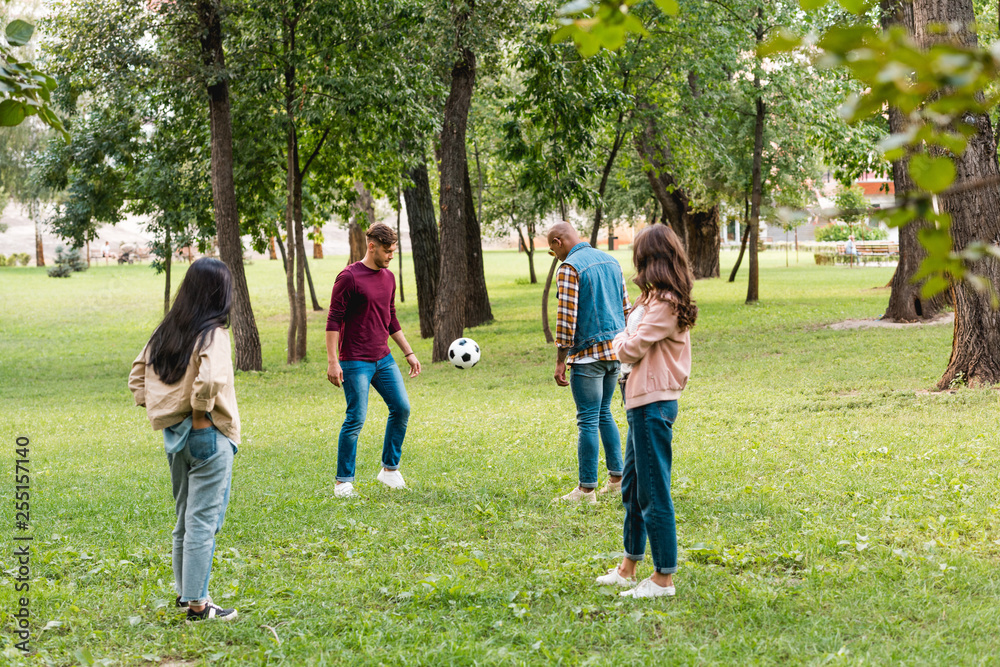 Fototapeta premium cheerful multicultural group of friends standing in park near football