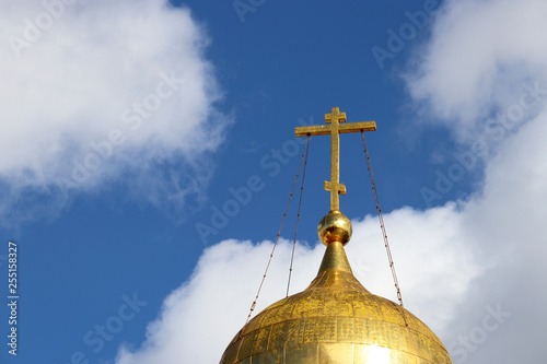 Golden dome of the Christian temple with a cross against the blue sky with white clouds. Orthodox church, background for religious greeting card