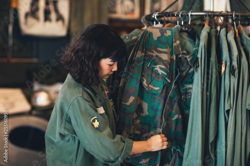 Pretty Asian woman standing by the clothes rack at vintage military shop and folding shirts. photo